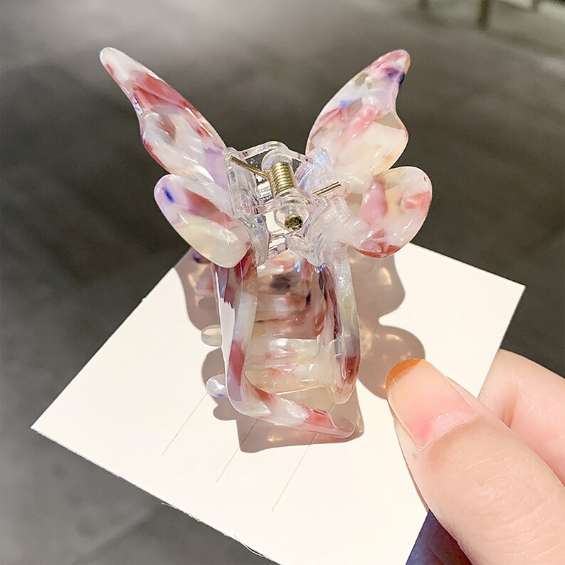 May include: A clear plastic butterfly hair clip with pink, white, and blue marbled accents. The clip has a spring mechanism to hold hair in place.