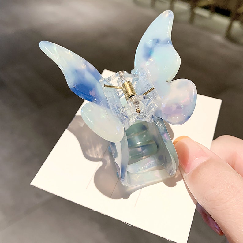 May include: A clear plastic butterfly hair clip with a blue and white marbled design.