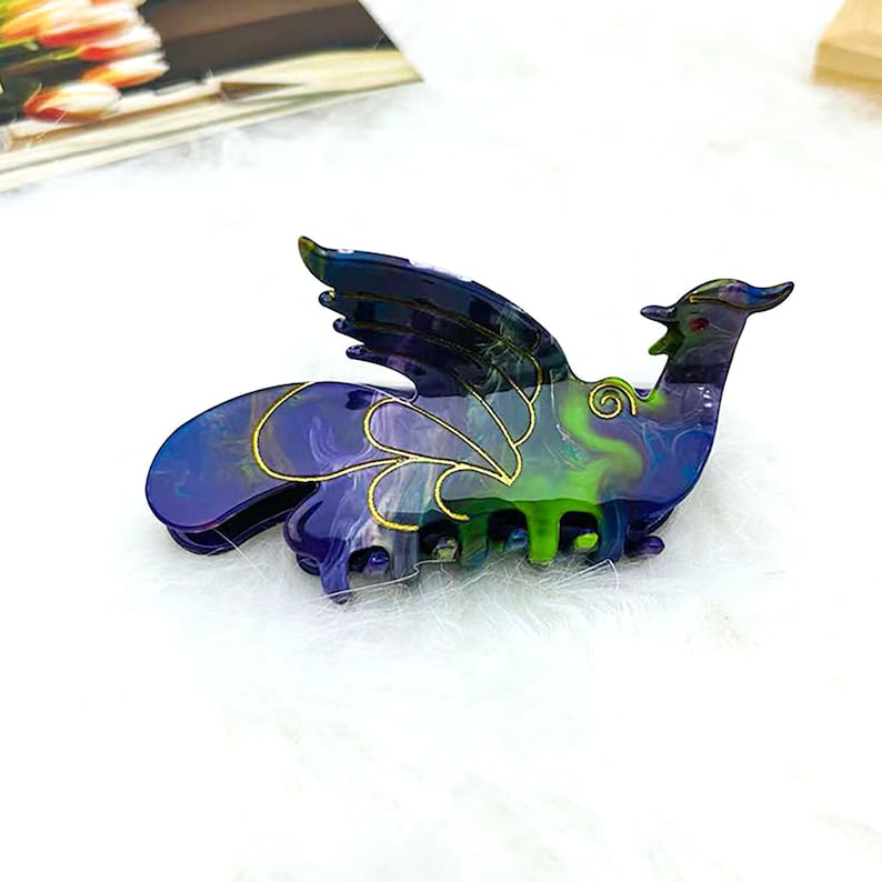 Peut inclure: Une pince &agrave; cheveux en forme de dragon de couleur violette et verte avec des accents dor&eacute;s. La pince a un motif en spirale et est en plastique.
