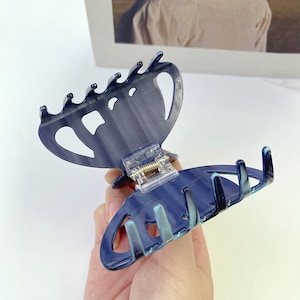 Puede incluir: Una pinza para el pelo de pl&aacute;stico azul con un patr&oacute;n de espiral. La pinza est&aacute; abierta y el mecanismo de resorte es visible.