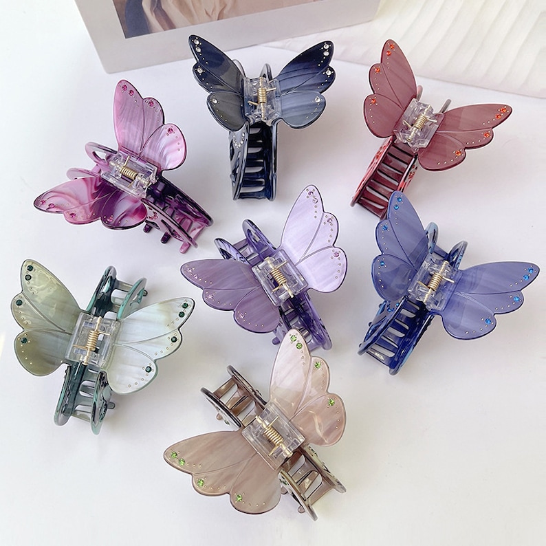 Puede incluir: Conjunto de seis pinzas para el pelo con forma de mariposa en varios colores, incluyendo morado, azul, verde y marr&oacute;n. Cada pinza presenta un dise&ntilde;o de mariposa detallado con pedrer&iacute;a.
