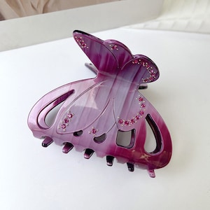 Puede incluir: Una pinza para el pelo de color morado con forma de mariposa con pedrer&iacute;a. La pinza tiene un acabado texturizado, iridiscente y un agarre fuerte.