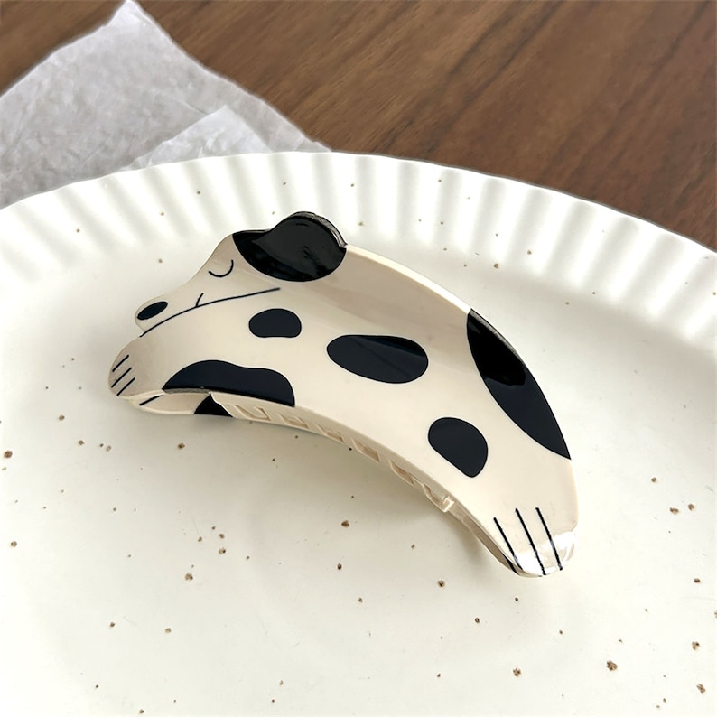 May include: A white and black spotted hair clip shaped like a sleeping dog. The clip is made of plastic and has a shiny finish.