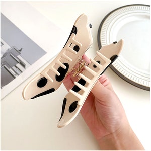 May include: A large, beige plastic hair claw with black polka dots. The claw has a spring-loaded hinge and a textured grip.