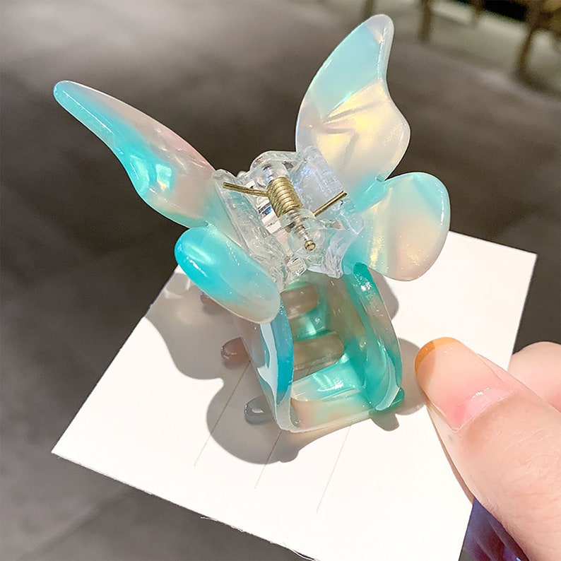 May include: A light blue butterfly hair clip with a clear plastic body and a gold spring. The clip is designed to hold hair in place.