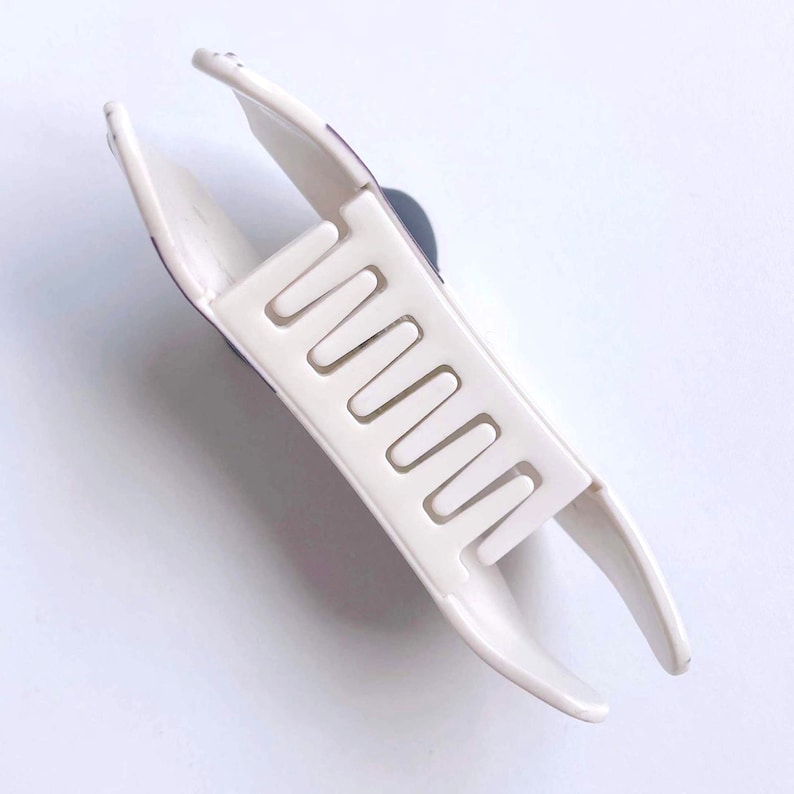 May include: White plastic hair claw with a textured surface and a row of teeth. The claw is open and ready to hold hair.