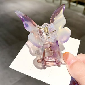 May include: A clear iridescent purple butterfly hair clip. The clip is made of plastic and has a spring-loaded mechanism.