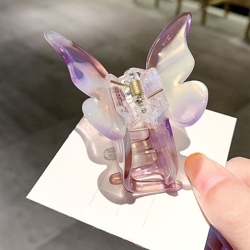 May include: A clear iridescent purple butterfly hair clip. The clip is made of plastic and has a spring-loaded mechanism.