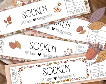 Op de afbeelding: Witte rechthoekige labels met het Duitse woord "SOCKEN" in zwart, versierd met herfstillustraties. De labels bevatten Duitse tekst, een hartsymbool en ruimte voor materiaalsamenstelling en wasvoorschriften.