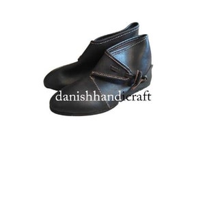 Könnte beinhalten: Schwarze Lederstiefel mit Knopfschluss und weißen Nähten. Die Stiefel haben eine abgerundete Spitze und einen niedrigen Absatz.