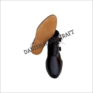 Könnte beinhalten: Ein Paar schwarze Lederstiefel mit Knopfschluss. Die Stiefel haben eine braune Ledersohle mit Nähten und eine spitze Zehenpartie.