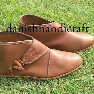 Könnte beinhalten: Ein Paar braune Lederstiefel mit Knöchelhöhe, schlichtem Design und Schnürung. Die Stiefel stehen auf grünem Gras. Der Text "danishhandicraft" ist auf dem Bild zu sehen.