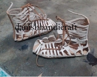 May include: A pair of handmade, open-toe leather sandals. The sandals are beige with brown leather straps and feature a cage-like design. The text "danishhandicraft" is visible on the image.