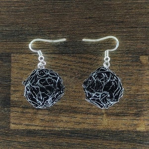 May include: A pair of black wire earrings shaped like a ball of yarn. The earrings are made of thin wire that is twisted and knotted together to create a spherical shape.