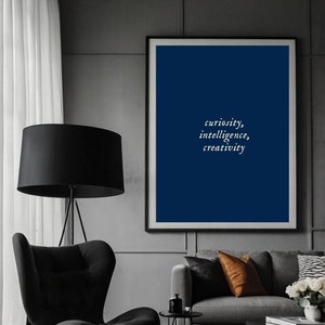 May include: A stylish living room featuring a black armchair, a floor lamp, and a framed print with the words "curiosity, intelligence, creativity" on a blue backdrop. A grey sofa with cushions and a black ottoman are also visible.