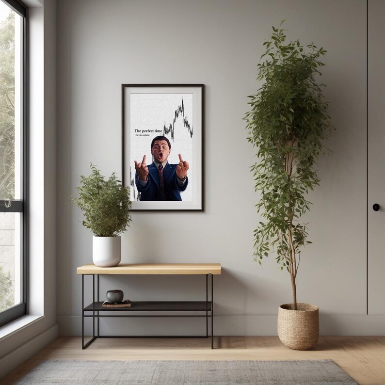 May include: A framed print featuring a man in a suit gesturing with both middle fingers up. The background shows a stock market graph. The text on the print reads "The perfect time, never settle."