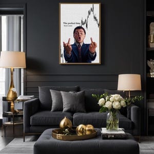 May include: A framed print featuring a man in a suit gesturing with both hands, with the text "The perfect time. Never comes." The print hangs above a dark gray sofa with gray pillows and a matching ottoman. A gold tray holds decorative spheres.