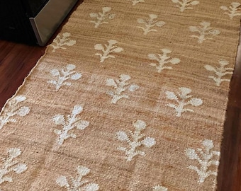 May include: A natural fiber rug with a white floral pattern on a beige background. The rug is woven with a textured, slightly rough surface.