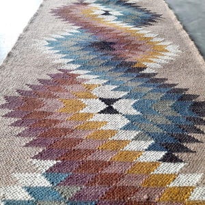 May include: A woven rug with a geometric pattern in shades of brown, blue, white, and gold. The rug has a natural, earthy feel and would add a touch of bohemian style to any room.