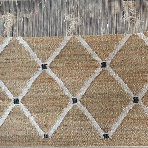 May include: A woven rug with a diamond pattern in white and black on a beige background.