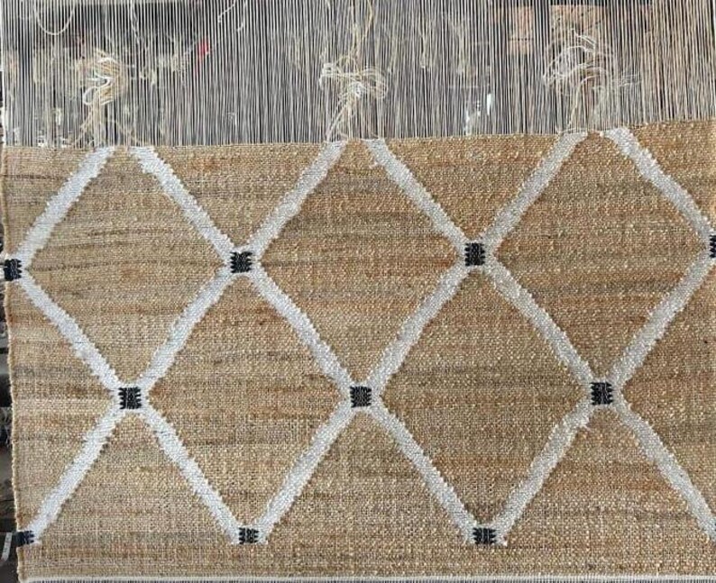 May include: A woven rug with a diamond pattern in white and black on a beige background.