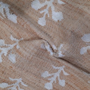 May include: A beige jute rug with a white floral pattern. The rug is woven with a textured surface and has a natural, earthy look.