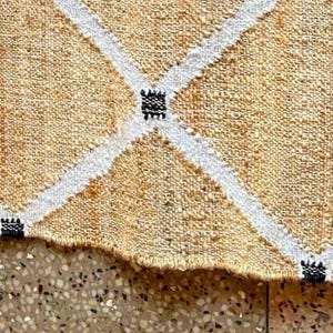 May include: A beige and white woven rug with a diamond pattern. The rug has black accents throughout the design.