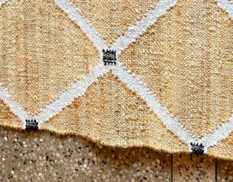 May include: A beige and white woven rug with a diamond pattern. The rug has black accents throughout the design.