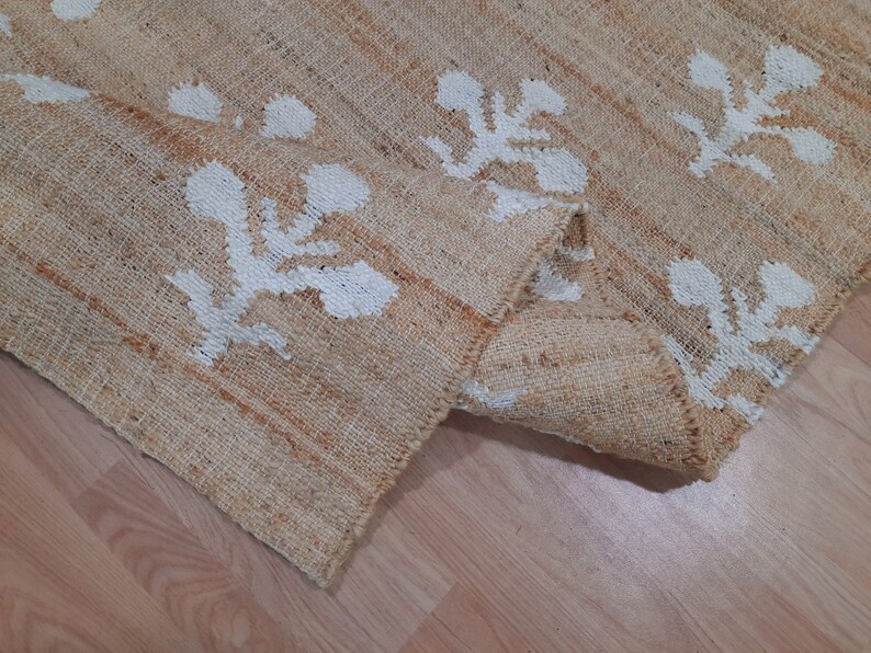 May include: A natural fiber rug with a beige background and white floral patterns. The rug is woven with a textured, slightly rough surface.