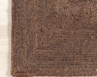 May include: Close-up of a brown woven jute rug with a textured surface. The rug has a square shape and a simple design.