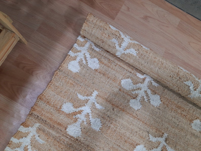 May include: A beige and white woven rug with a floral pattern. The rug is rolled up and the pattern is visible on the rolled up portion.