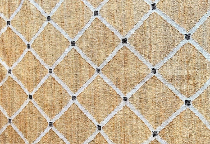 May include: A beige rug with a white diamond pattern and black accents. The rug is woven with a textured, natural fiber.