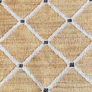 May include: A beige woven rug with a diamond pattern in white and black. The rug has a natural, rustic look.