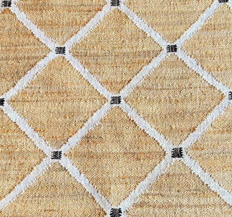 May include: A beige woven rug with a diamond pattern in white and black. The rug has a natural, rustic look.