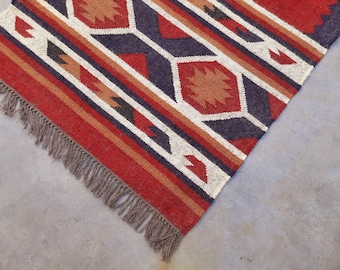 May include: A red, white, and blue patterned rug with fringe. The rug has a geometric design with a diamond pattern.