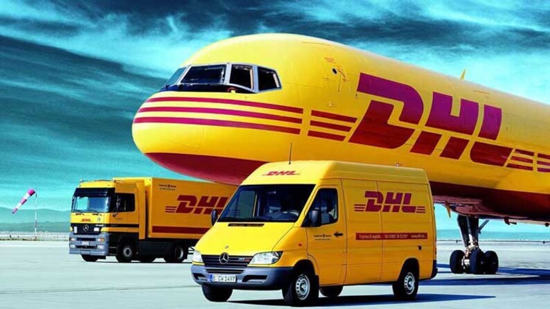 May include: A yellow DHL cargo plane with a red stripe and the DHL logo on the side. A yellow DHL delivery truck and a yellow DHL van are parked in front of the plane.