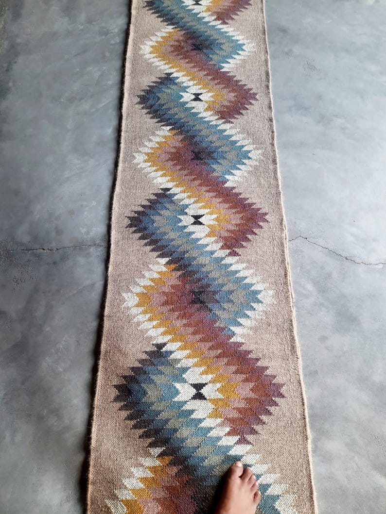 May include: A long, narrow rug with a geometric pattern in shades of blue, brown, white, and yellow. The rug has a woven texture and is made of natural fibers.