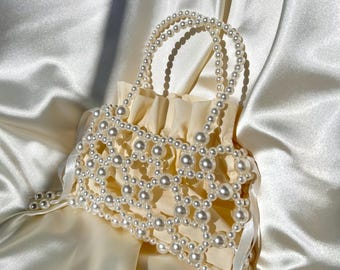 May include: A white pearl beaded bag with a drawstring closure and a long strap. The bag is made of a delicate pearl mesh and has a soft, feminine look.