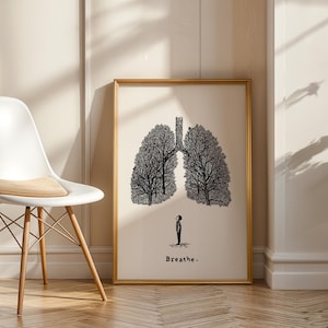May include: A framed art print featuring a black and white illustration of lungs shaped like trees, with a small figure beneath. The word "Breathe" is printed below the figure. The artwork is displayed in a room with a white chair.