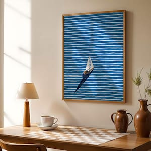 Puede incluir: Una obra de arte enmarcada con un velero sobre un fondo azul con l&iacute;neas horizontales blancas. La obra de arte est&aacute; en un marco de madera. Tambi&eacute;n se ven una mesa de madera, una l&aacute;mpara, una taza de caf&eacute; y jarrones.