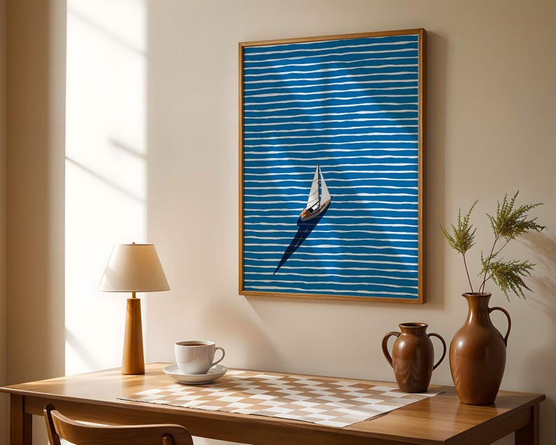 Puede incluir: Una obra de arte enmarcada con un velero sobre un fondo azul con l&iacute;neas horizontales blancas. La obra de arte est&aacute; en un marco de madera. Tambi&eacute;n se ven una mesa de madera, una l&aacute;mpara, una taza de caf&eacute; y jarrones.