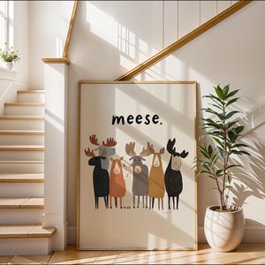 Könnte beinhalten: Ein gerahmter Kunstdruck mit einer Gruppe stilisierter Elche in verschiedenen Farben. Das Wort "meese" ist über den Elchen aufgedruckt. Das Kunstwerk wird in einem hellen Flur mit einer Treppe und einer Topfpflanze ausgestellt.