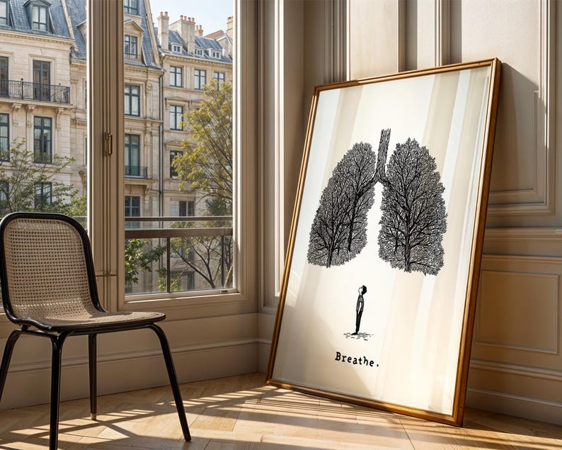 May include: A framed art print featuring a black and white illustration of lungs resembling trees, with a small figure below. The print is leaning against a wall, with the word "Breathe" at the bottom. A chair sits near a window.