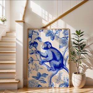 May include: A framed wall art print featuring a blue monkey illustration on a cream background, surrounded by blue floral patterns. The artwork is displayed in a bright, well-lit interior setting, leaning against a wall.