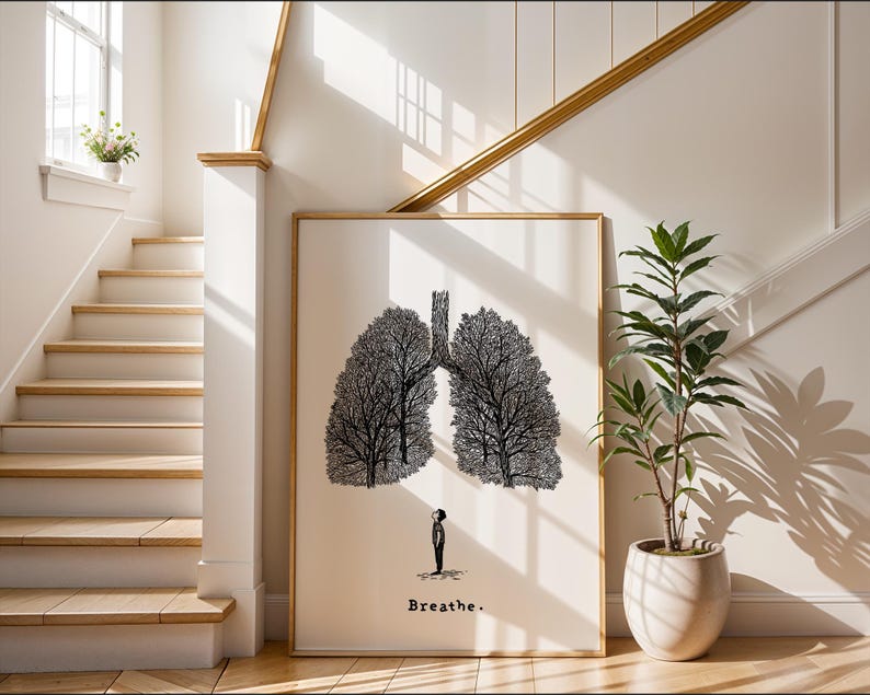 May include: A framed art print featuring a black and white illustration of lungs shaped like trees, with a small figure beneath. The word "Breathe" is written at the bottom. The artwork is displayed in a bright, airy space with a staircase and a potted plant.