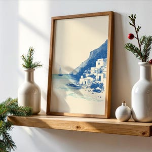 May include: A framed print of a coastal scene in blue and white tones, depicting a village on a cliffside. The print is displayed on a wooden shelf, alongside decorative vases and a small ornament. The overall theme is coastal decor.