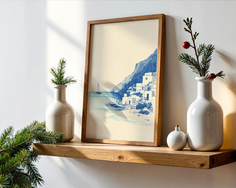 May include: A framed print of a coastal scene in blue and white tones, depicting a village on a cliffside. The print is displayed on a wooden shelf, alongside decorative vases and a small ornament. The overall theme is coastal decor.