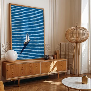 Puede incluir: Una impresi&oacute;n art&iacute;stica abstracta azul y blanca enmarcada de un velero sobre el agua cuelga sobre un mueble de madera. Una l&aacute;mpara esf&eacute;rica blanca y una l&aacute;mpara de pie decorativa de madera tambi&eacute;n est&aacute;n en la habitaci&oacute;n. La habitaci&oacute;n tiene un dise&ntilde;o moderno y minimalista.