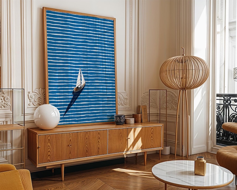 Puede incluir: Una impresi&oacute;n art&iacute;stica abstracta azul y blanca enmarcada de un velero sobre el agua cuelga sobre un mueble de madera. Una l&aacute;mpara esf&eacute;rica blanca y una l&aacute;mpara de pie decorativa de madera tambi&eacute;n est&aacute;n en la habitaci&oacute;n. La habitaci&oacute;n tiene un dise&ntilde;o moderno y minimalista.