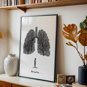 May include: Black framed art print featuring a stylized illustration of lungs formed by trees. A small figure stands below the lungs, with the word "Breathe" printed beneath. The artwork is displayed on a white wall, with a wooden shelf above.